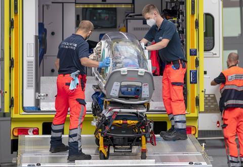 A photo of emergency staff with an isolation pod and an ambulance