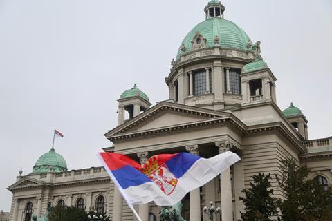 An image showing a Serbian flag in front of the Serbian Parliament building