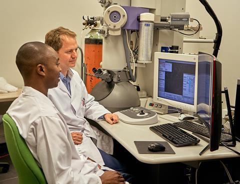 An image showing Dr Mulelu and Dr Woodward in front of the cryo-electron microscope at UCT 