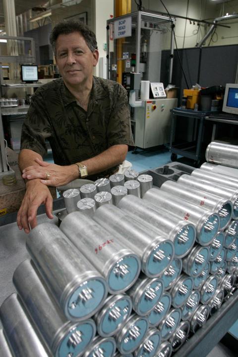 A man stands by a rack of silver supercapacitor units, around the size of a 500ml drink can