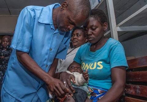 An image showing a health surveillance assistant giving a malaria vaccine dose to a toddler