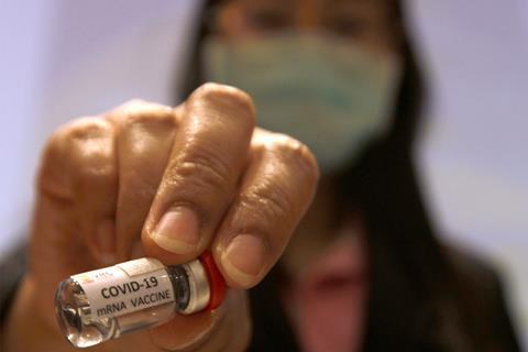 A photo of a woman holding a vial labelled COVID-19 mRNA vaccine