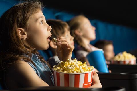 Little girl looking fascinated eating popcorn watching a movie at the movie theatre.