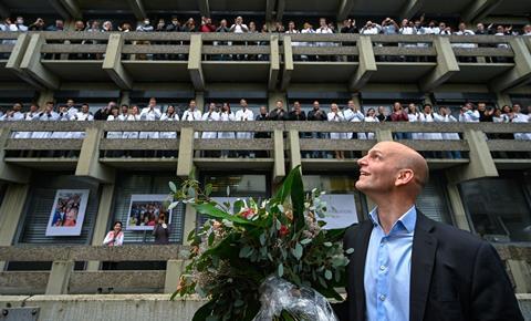 An image showing Benjamin List looking up at a large group of researchers in balconies