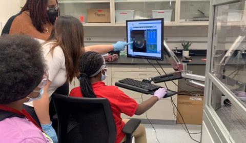 Scientists helping middle school students to use a computer in a professional lab