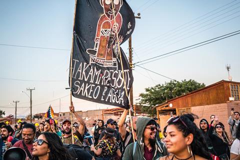 A photo showing a large group of people under a blue sky holding up a banner that says 'Takami resiste sakeo del agua'