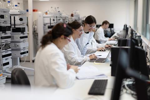 Scientists in lab coats and goggles working at laptop computers in a lab