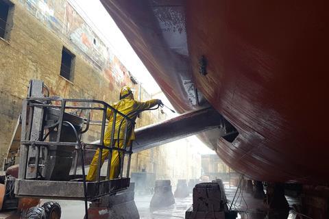 Worker washing ship hull at drydock