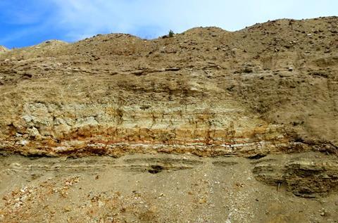 A sandy coloured cliff with horizontal stripes of white and orange minerals