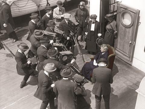 Marie Curie (circa 1915) standing in front of a group of cameramen on board a ship