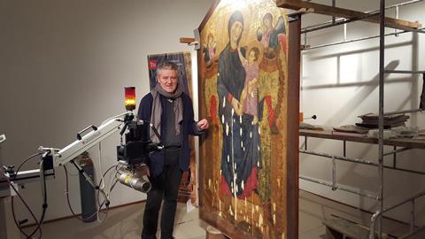 Rocco Mazzeo standing by a painting he is restoring