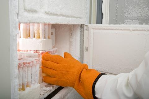 An image showing a gloved hand touching chemical samples from a freezer