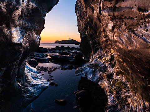 View toward Godrevy Island and lighthouse from inside a cave at sunset. Cornwall, England