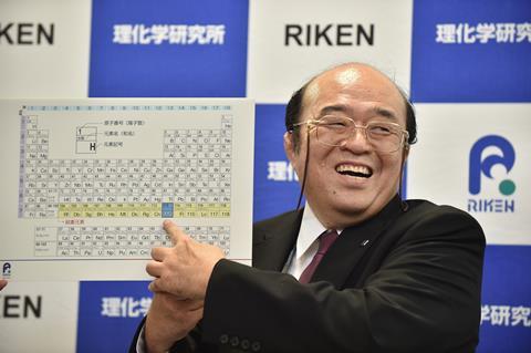 An image showing Kosuke Morita smiling and pointing at element 113