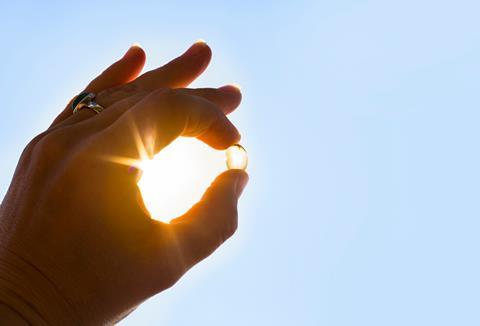 Hand holding a vitamin d capsule infront of the sun 