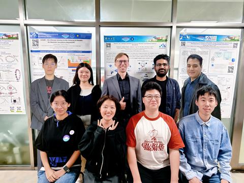 A team of scientists posed in rows for a group shot in front of some scientific researcher posters