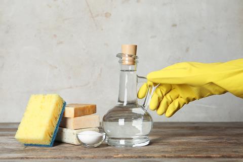 Gloved hand reaching for a bottle of vinegar and cleaning supplies