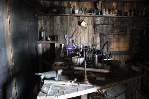 Apparatus and an array of historical instruments crowd a wooden bench at the Physical Lab at Cape Evans, 2019-2020