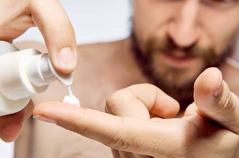 A man with a beard squeezes out skin care cream