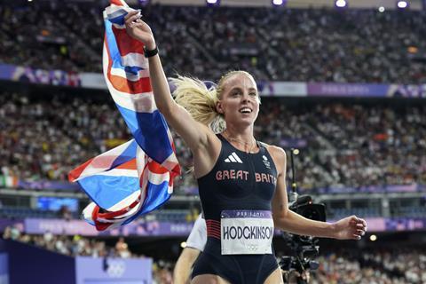 A female athlete waves a flag after winning a race in a large stadium full of people