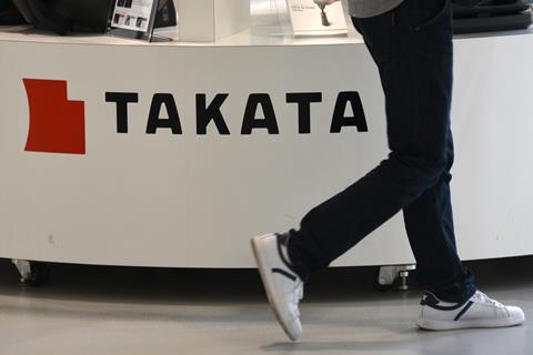 Visitor walking past Takata sign in vehicle showroom - original