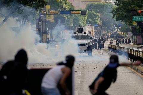 Protesters throwing items at an armoured vehicle screened by smoke bombs