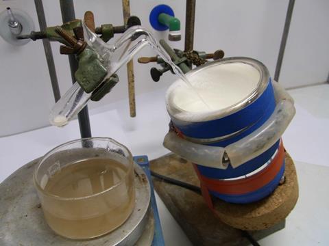 An image showing the synthesis of hydrazoic acid. On the left, there's a glass vial being heated in an oil bath, on the left, a glass tube connects the vial to a thin glass capillary held in a Dewar containing liquid nitrogen.
