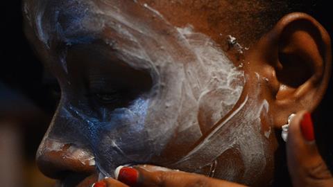 Closeup photo of a woman with dark skin applying white skin lightening cream to her face
