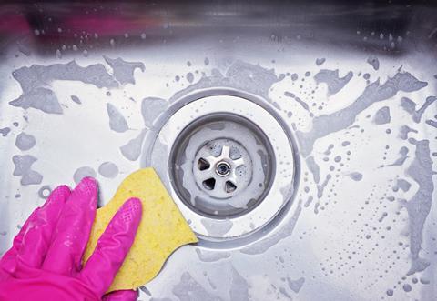 Close up sink drain and hand wearing pink rubber glove cleaning scrub steel sink with sponge