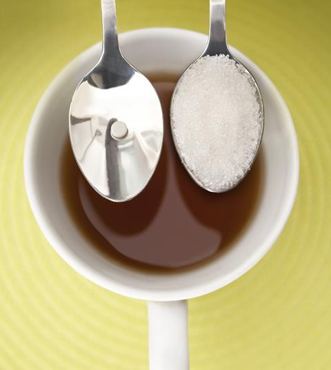 An image showing two spoons, one containing a sugar substitute, and one containing sugar