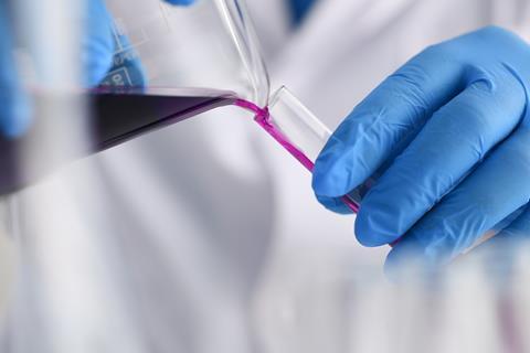 Gloved hand pouring potassium permanganate into a test tube